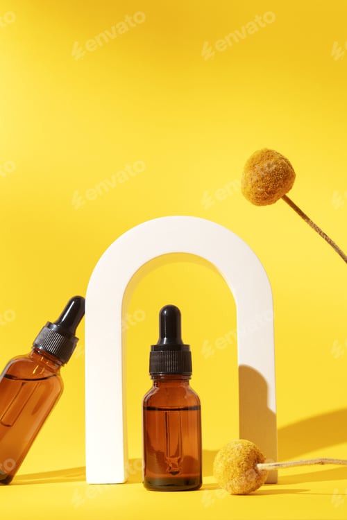 Preview: Two bottles different size with serum in arch with floral extracts craspedia flowers.