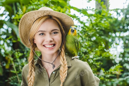 Preview: happy young woman in safari suit with parrot on shoulder in jungle