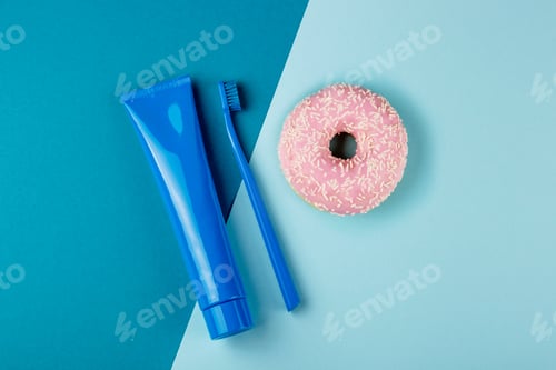Preview: Blue tube of toothpaste blue toothbrush and pink donut lie on combined blue background. Top view