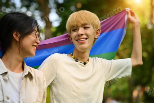 Preview: Male and female LGBT friends holding and raising a rainbow flag.