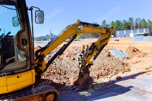 Preview: Excavator digging earth at a construction site in warm sunlight with trees in the background