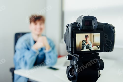Preview: Young handsome blogger with a camera filming himself in a room