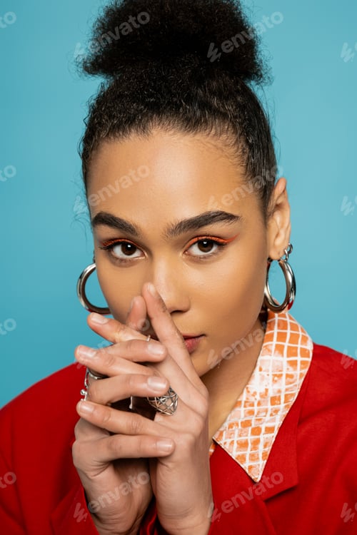 Preview: portrait of african american model in silver accessories and vibrant outfit posing on blue backdrop