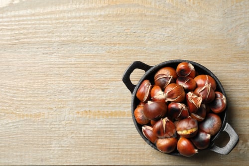 Preview: Tasty roasted edible chestnuts on wooden table, top view. Space for text
