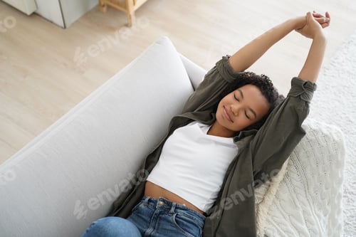 Preview: Relaxed biracial young girl lying on cozy couch at home stretching, waking up after napping break