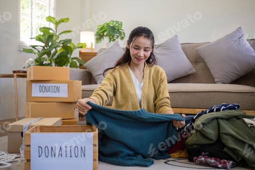 Preview: A young Asian woman sits on a sofa sorting unwanted clothes to donate to a charity.