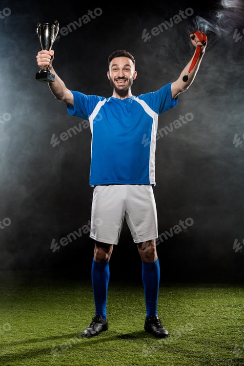 Preview: happy champion holding trophy and medals in hands on black with smoke