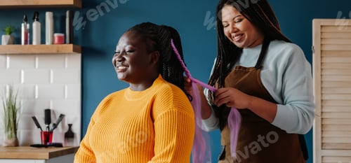 Preview: Happy African American hairdresser braiding hair to a female customer in salon