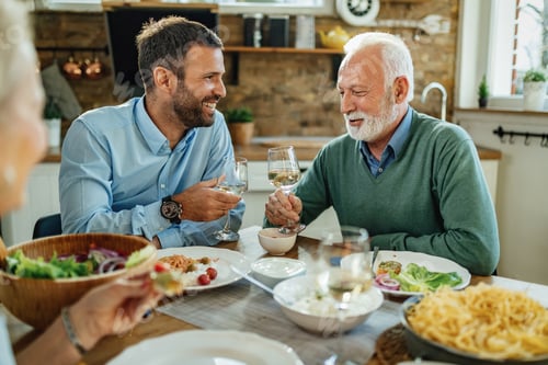 Preview: Happy senior man and his son toasting with wine at dining table.