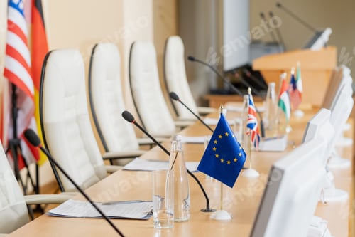 Preview: Row of microphones, flags, papers and other on long table in conference hall