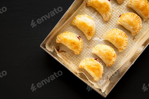 Preview: Homemade Cherry Hand Pies in a baking pan on a black background, top view. Space for text.