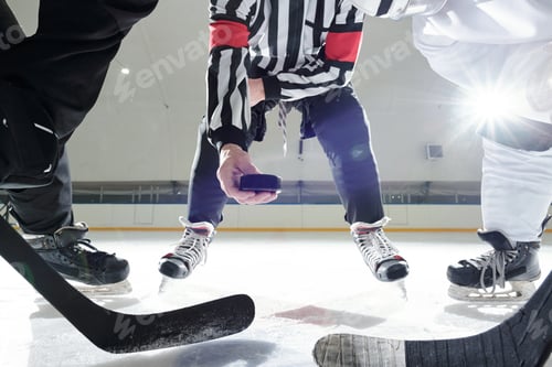 Preview: Hockey referee with puck standing on ice rink between two players with sticks
