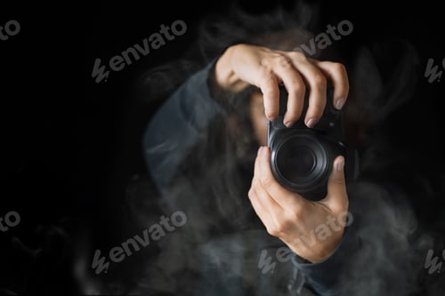 Preview: Woman's hands held photo camera. Close up shot. A person in black hoodie and smoke around