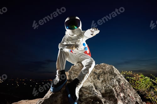 Preview: Space traveler sitting on rocky mountain under night sky.
