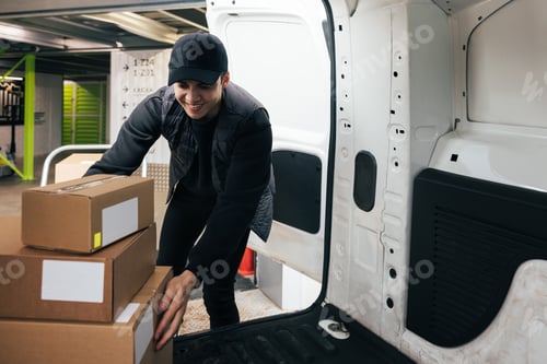 Preview: Smiling male courier working in warehouse upload boxes into a van for delivery