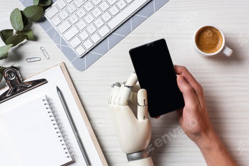 Preview: partial view of businessman with cyborg hand using smartphone with blank screen at table with coffee