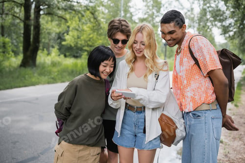 Preview: blonde woman searching location on smartphone near cheerful multiethnic friends