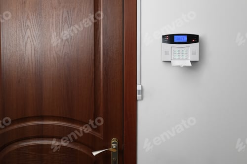Preview: Home security alarm system on white wall near door, space for text