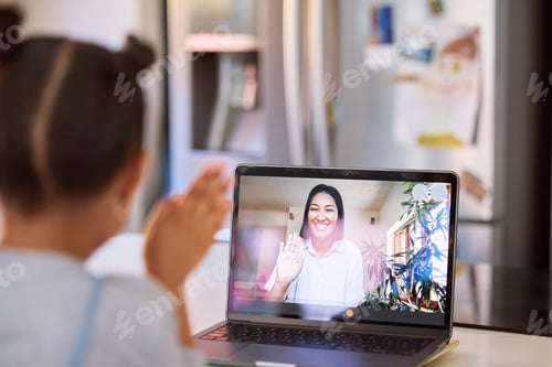 Preview: Little girl waving to greet on a video call with her smiling teacher, tutor or parent via webcam on