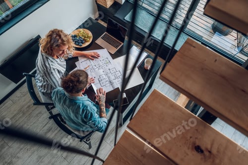 Preview: Happy couple using laptop and looking into blueprints of their new home