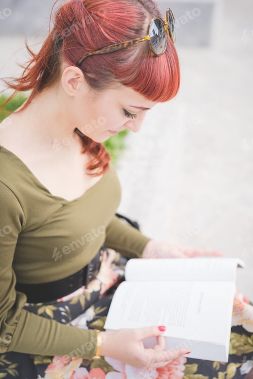 Preview: Half length of young handsome reddish pin up italian girl looking downward reading a book
