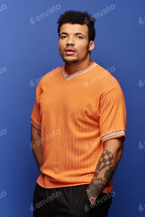 Preview: Handsome man posing in an orange shirt against a vibrant blue backdrop with confidence and style