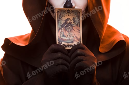 Preview: KYIV, UKRAINE - APRIL 18, 2019: cropped view of woman with skull makeup holding tarot card isolated