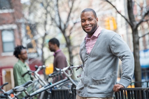 Preview: Outdoors in the city in spring. A man using leaning on a railing by a cycle rack.