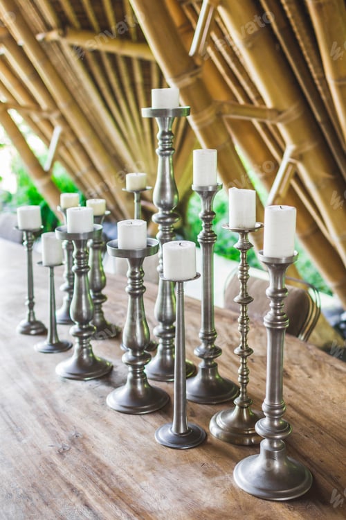 Preview: Many white candles in vintage metal candlesticks on wooden table as decoration of restaurant