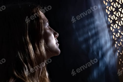 Preview: Close-up portrait of a young woman with shadows and light on her face from rays from the window