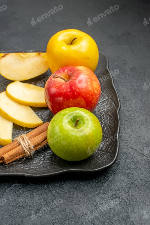 Preview: Vertical view of several types of sliced and whole fresh apples on a black tray and cinnamon limes