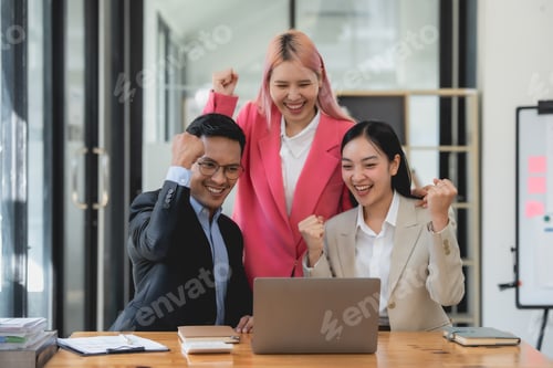 Preview: Triumphant asian business team with raised fists celebrating success at the office.