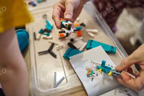 Preview: the hands of an adult assemble parts of a plastic designer according to the instructions, a children