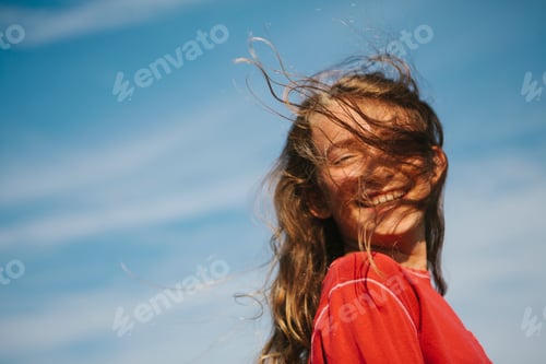 Preview: A smiling nine year old girl, with the wind blowing her hair over her face.