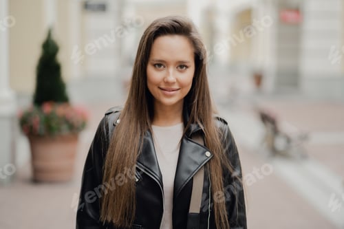 Preview: Portrait of a stylish young woman in a leather jacket smiling on a city street.
