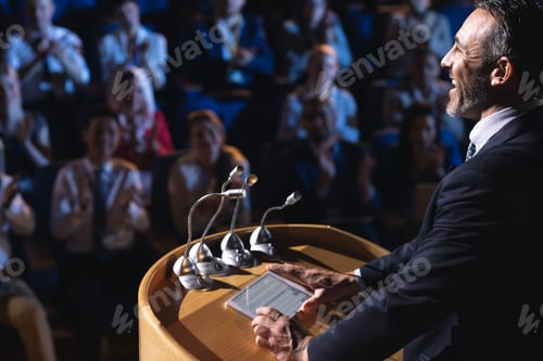 Preview: Side view of Caucasian businessman standing and giving presentation in the auditorium