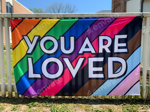 Preview: You are loved written on a progress pride flag integrated in one flag hanging on a fence