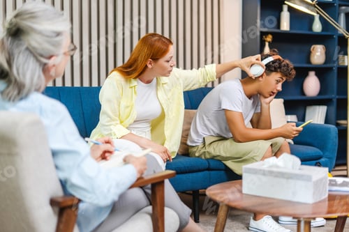 Preview: Mother removing headphones from teenage son using smartphone during therapy session