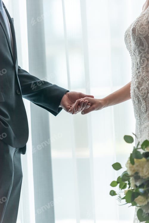 Preview: Vertical shallow focus shot of the groom holding the hand of the bride