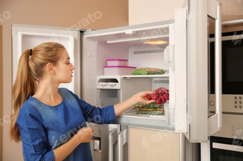 Preview: Young woman with frozen cherries near open refrigerator at home