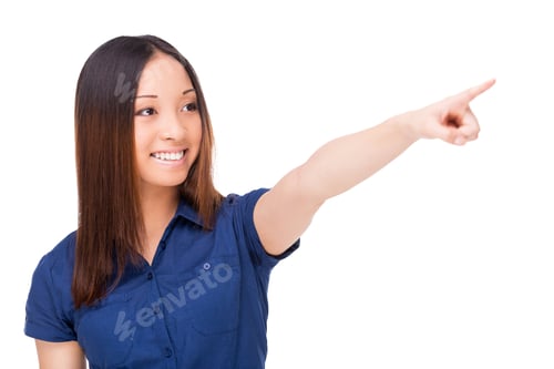 Preview: Over there! Beautiful young Asian woman pointing away and smiling while standing isolated on white