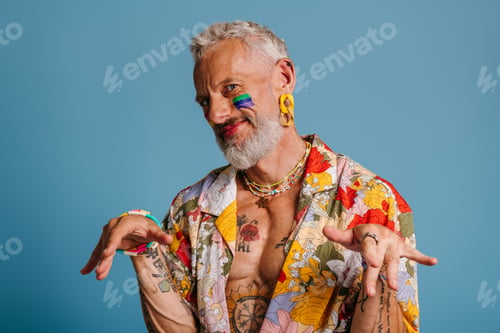 Preview: Mature gay man with rainbow flag make-up stretching out hand and smiling against blue background