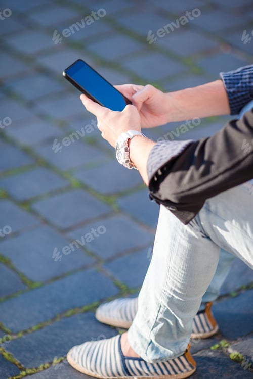 Preview: Closeup of male hands is holding cellphone outdoors on the street. Man using mobile smartphone