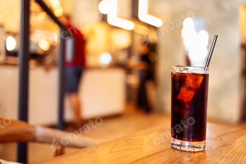 Preview: Glass of delicious coffee with ice cubes and a straw on a wooden backdrop.