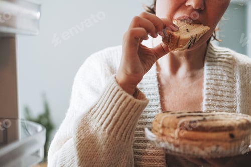 Preview: Attractive friendly brunette woman middle age in cozy cardigan eating cake from refrigerator