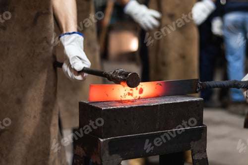 Preview: Blacksmith in gloves hot hitting metal part on anvil
