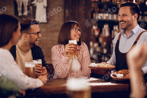 Preview: Cheerful waiter serving food to his guests in a pub.