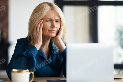 Preview: Stressed mature businesswoman having headache while working on laptop, woman looking at screen and