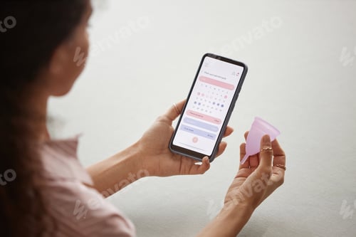 Preview: Closeup of woman holding phone and menstrual cup