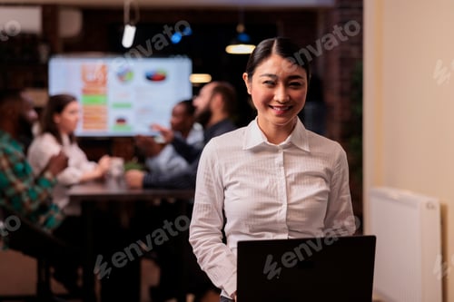 Preview: Portrait of smiling asian business employee holding laptop in startup office working overtime